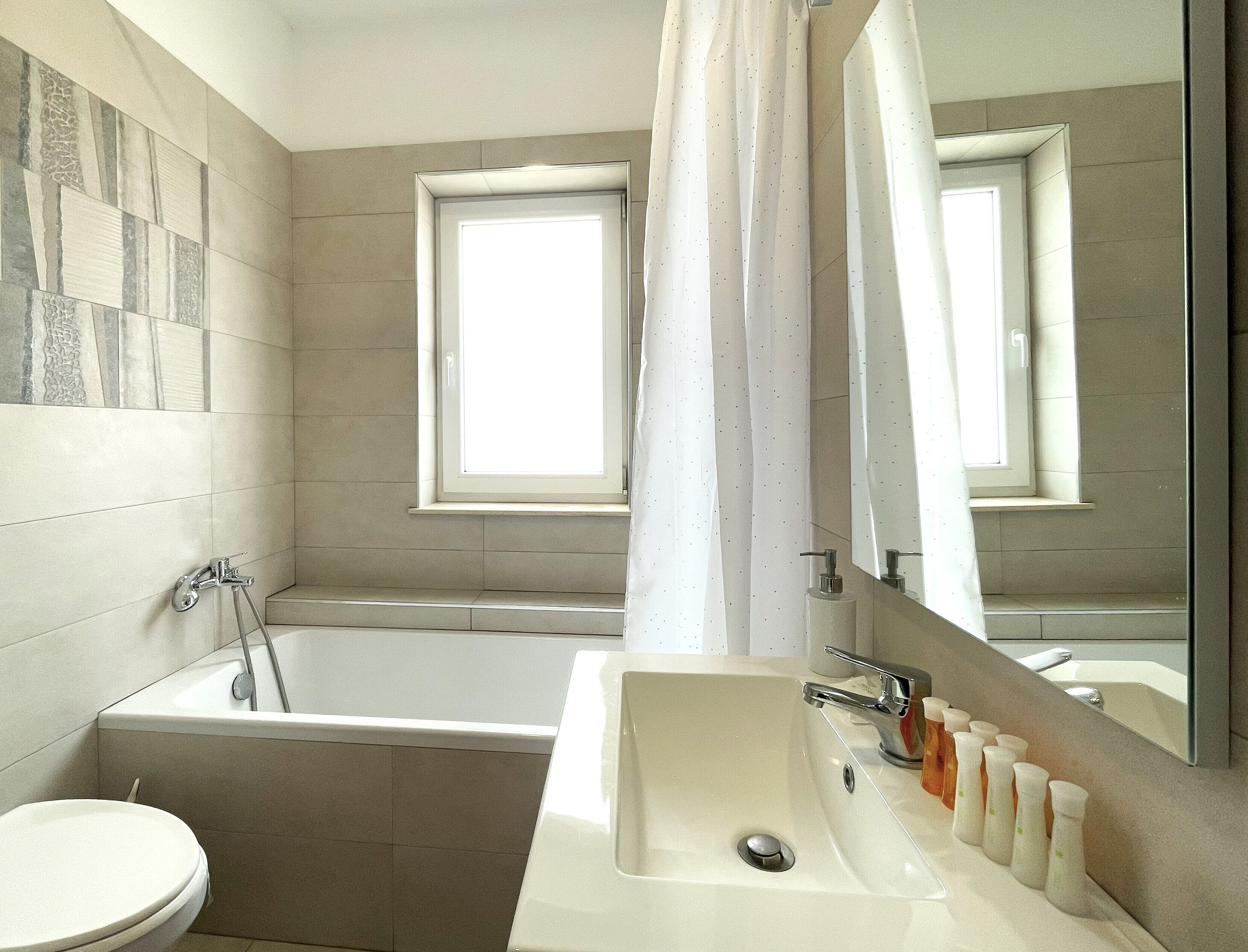 Ein modernes Badezimmer mit Badewanne, Waschbecken mit Seifenflaschen, Toilette und einem Fenster mit Blick.