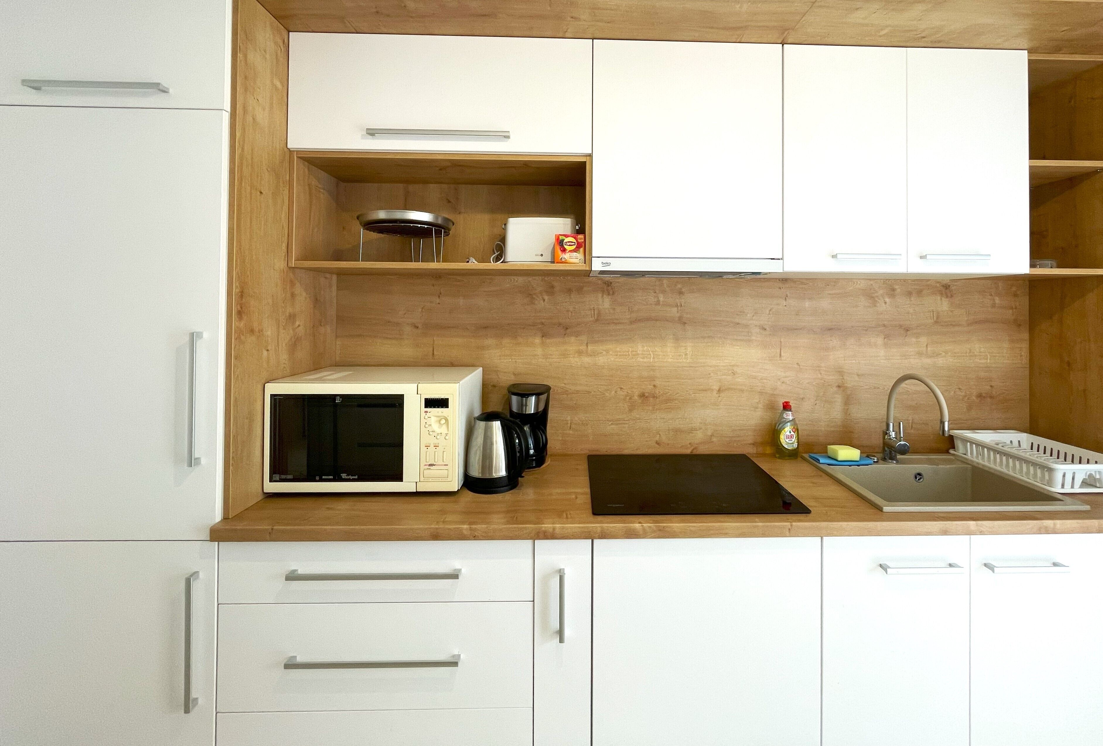 A compact kitchen with white cabinets, a microwave, a coffee maker, and a sink.