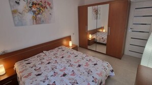 Ein Schlafzimmer mit einem Bett, einem Kleiderschrank, einem Nachttisch und einem an der Wand befestigten Spiegel.