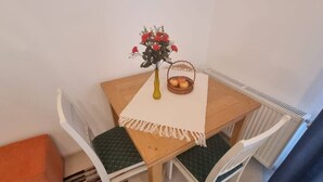 Ein kleiner Essbereich mit einem Holztisch, einer Blumenvase und einer Fruchtkorb.