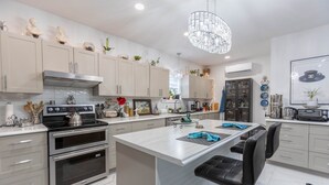 A modern kitchen with stainless steel appliances, a central island with bar stools, and decorative items on the cabinets. - Pleasant Street Inn (Parrsboro)