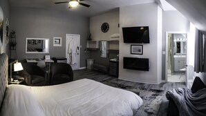 A hotel room with a large bed, a desk, a chair, a TV, a clock, and a bathroom visible through an open door. - Pleasant Street Inn (Parrsboro)