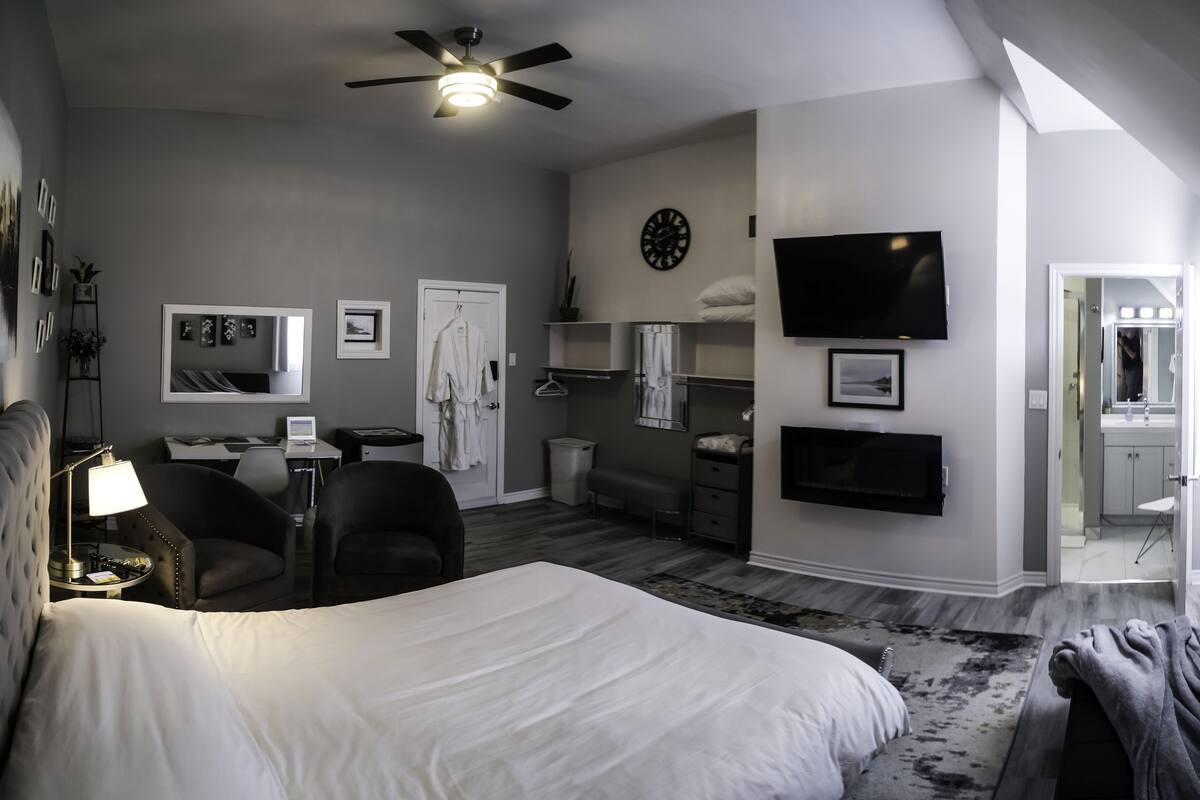 A hotel room with a large bed, a desk, a chair, a TV, a clock, and a bathroom visible through an open door.