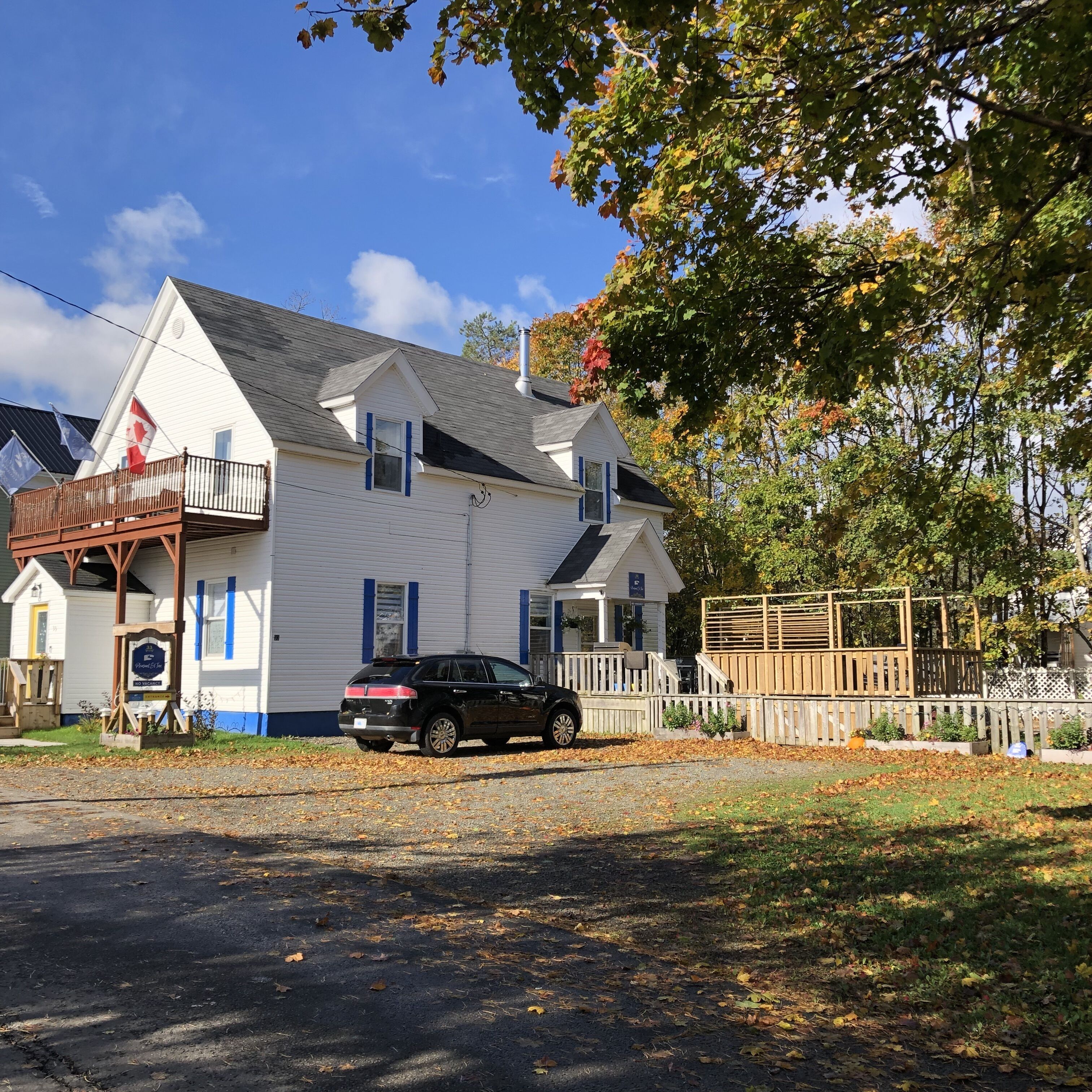 A white two-story house with a balcony, a black SUV parked in front, and a wooden fence.