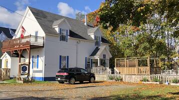 A white two-story house with a balcony, a black SUV parked in front, and a wooden fence.
