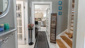 A hallway with a black patterned rug, a wooden sign with motivational quotes, and a staircase leading to a second floor. - Pleasant Street Inn (Parrsboro)