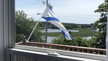 Un balcon d’où l’on aperçoit un drapeau, une balustrade et une étendue d’eau en arrière-plan.