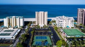 Un complejo hotelero frente al mar con varias torres, una cancha de tenis y un estacionamiento.