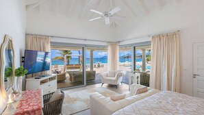 A spacious bedroom with a large bed, a TV, and a view of the beach.