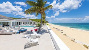 A beachfront resort with a pool area, lounge chairs, and a palm tree.