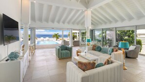 A spacious, well-lit living area with a view of the ocean, a pool, and a modern interior design.
