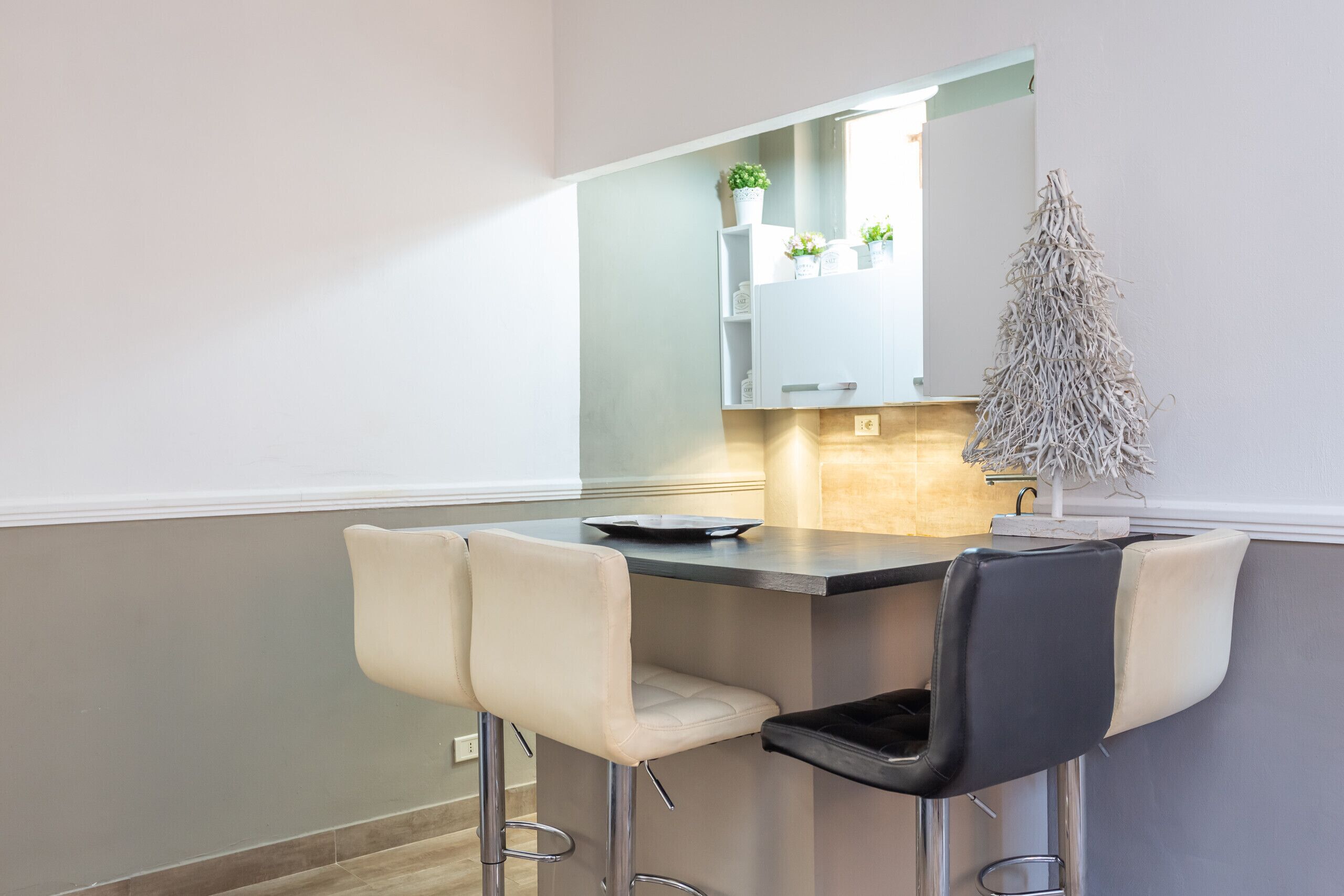 Una cocina moderna con barra, armarios blancos y un pequeño árbol decorativo.