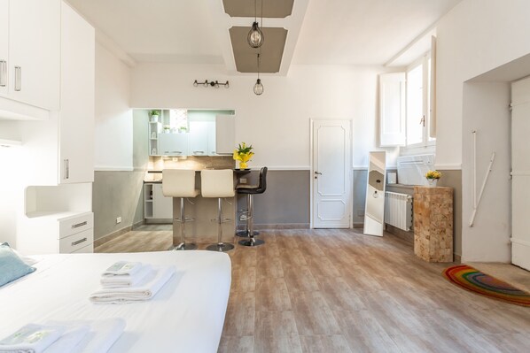 A modern hotel room with a large bed, a small kitchenette, a bathroom, and a dining area.
