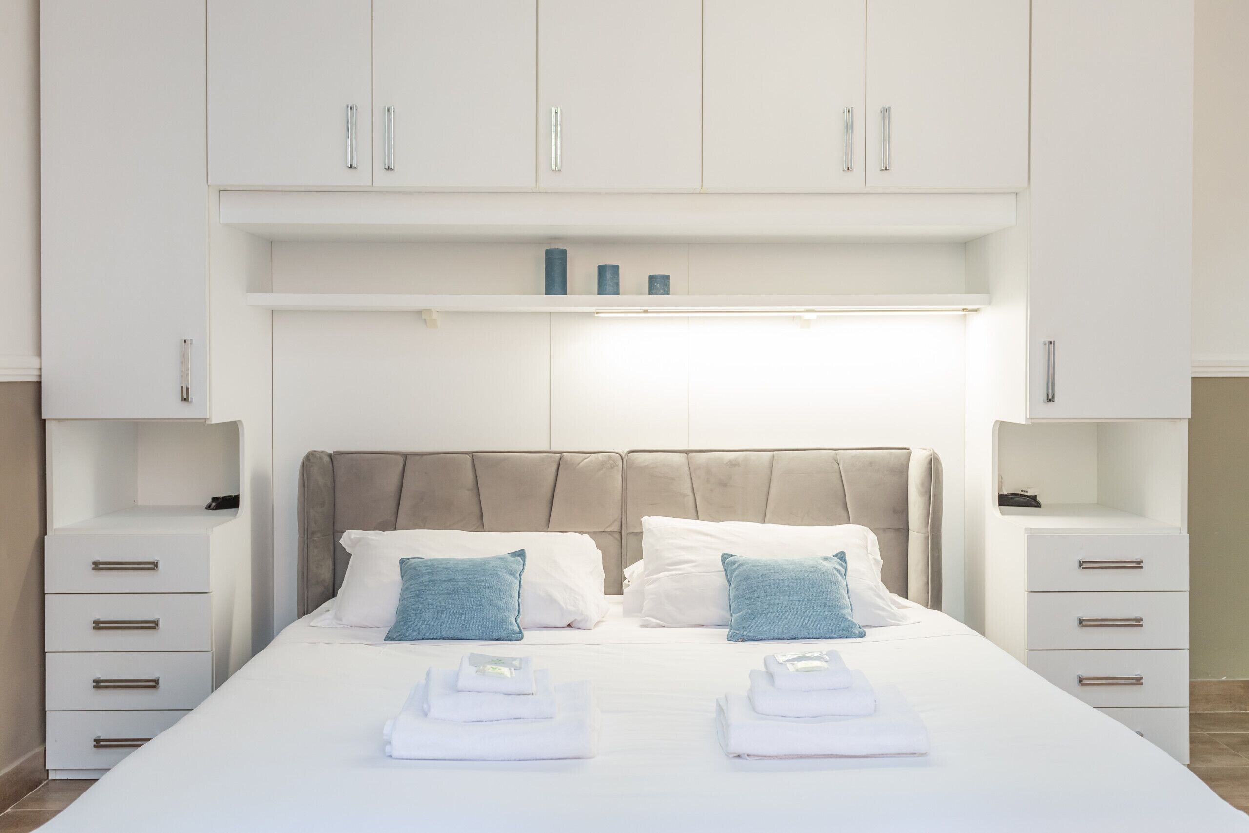 A hotel room with a large bed, two bedside tables, a wardrobe, and a shelf with toiletries.