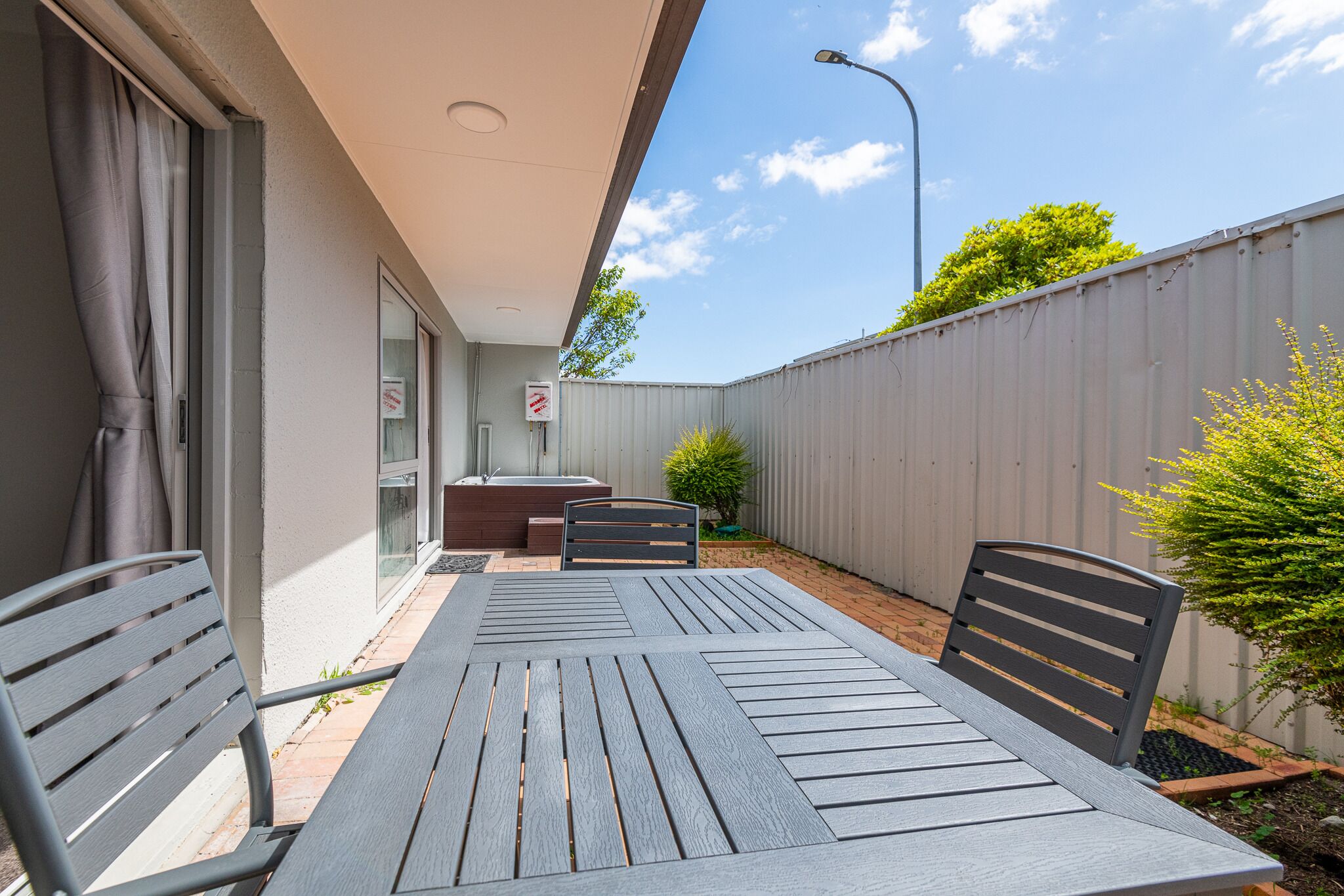 An outdoor patio with a table and chairs, a small seating area, and a view of the sky and trees.