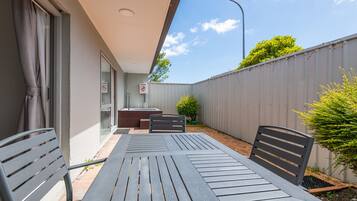 An outdoor patio with a table and chairs, a small seating area, and a view of the sky and trees.