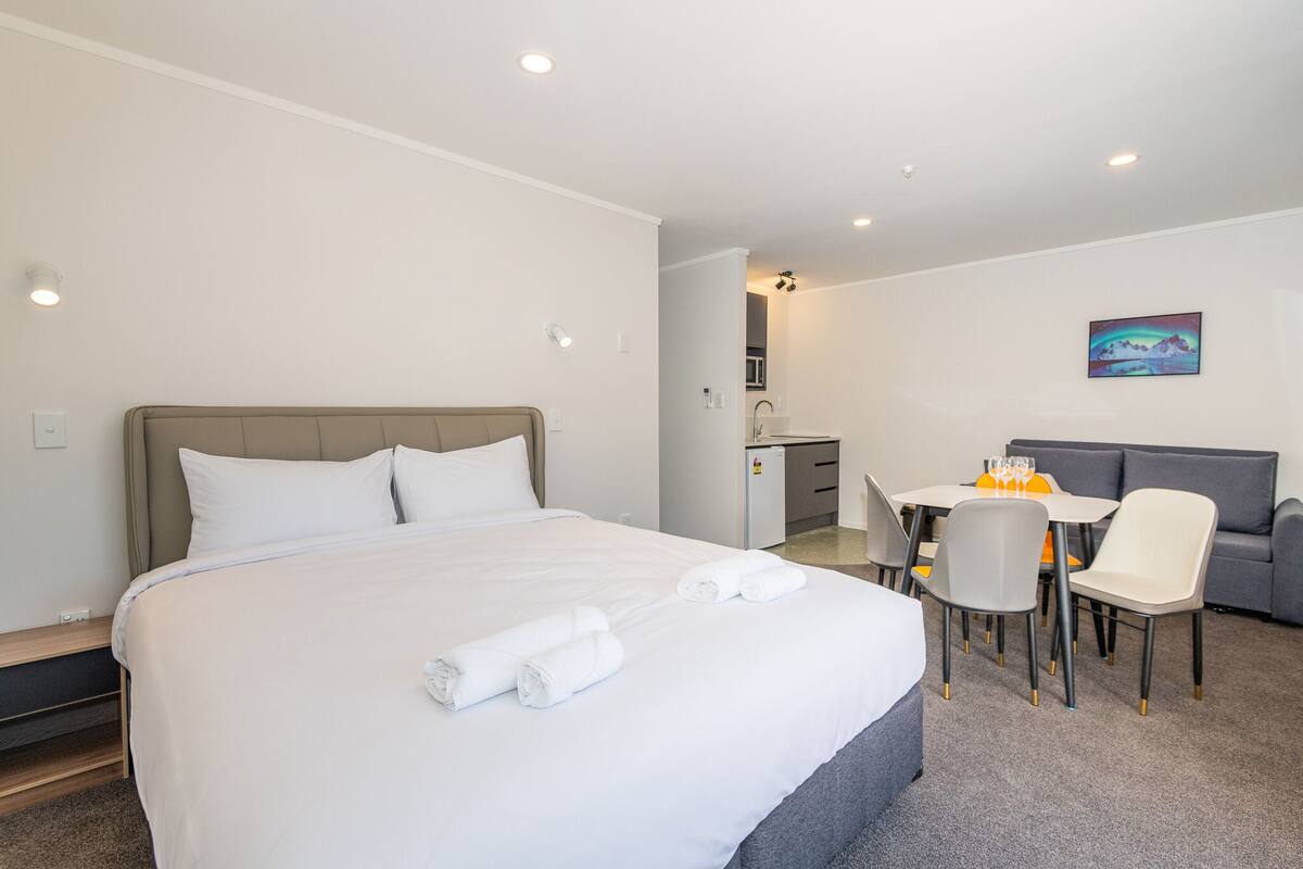 A hotel room with a bed, a desk, a chair, a sofa, and a painting on the wall.
