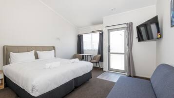 A hotel room with a bed, a desk, a chair, a TV, and a window with curtains.