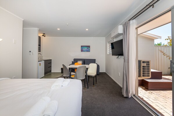 A hotel room with a bed, a desk with a chair, a TV, and a sliding glass door to a balcony.