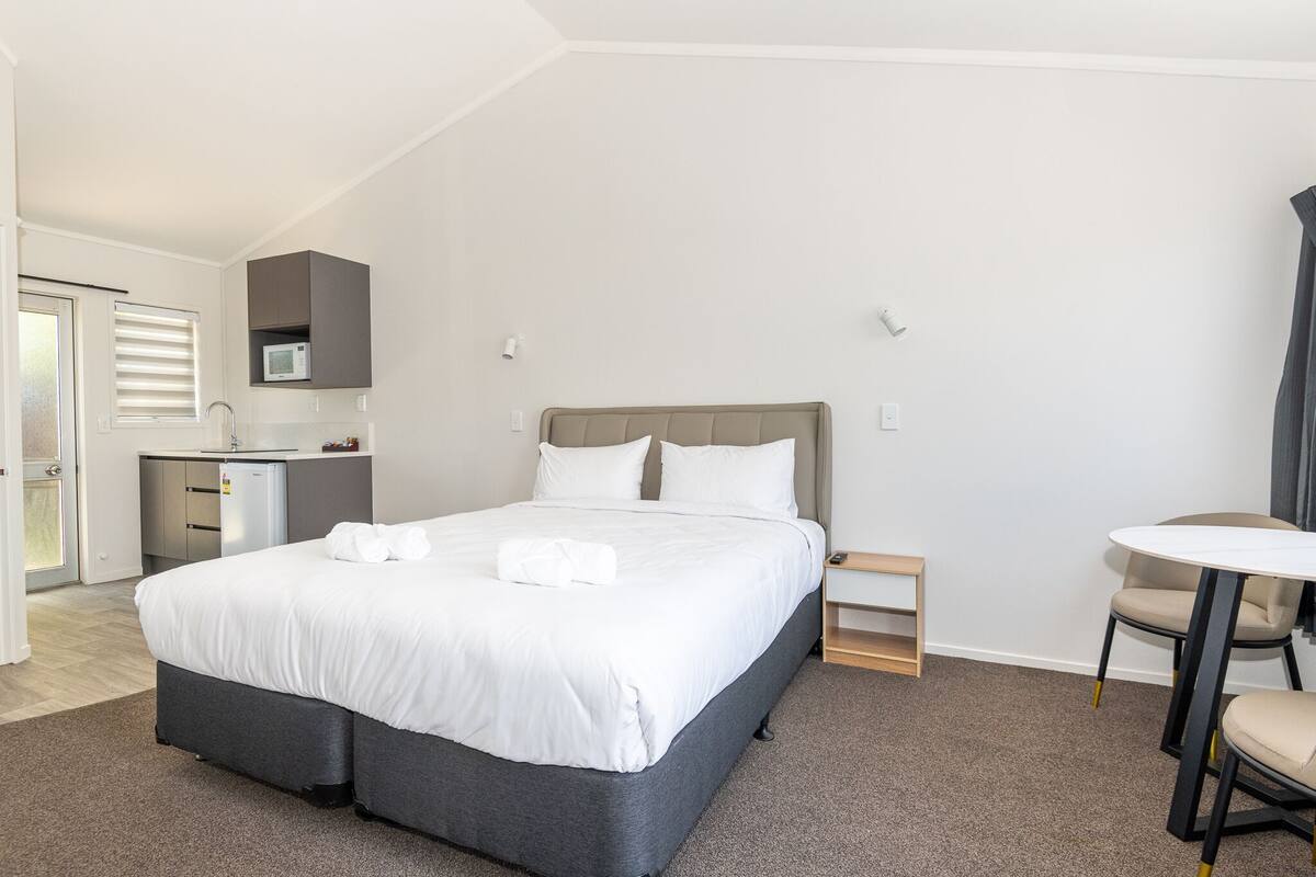 A hotel room with a bed, a small desk, a chair, a microwave, and a door leading to a bathroom.