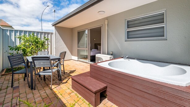 A patio with a hot tub, outdoor seating, and a sliding glass door leading to a bedroom. - Aurora City Suites Motel (Rotorua)
