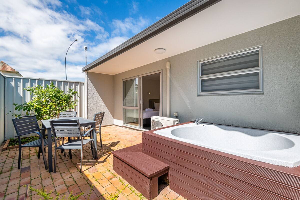 A patio with a hot tub, outdoor seating, and a sliding glass door leading to a bedroom.
