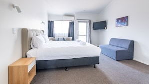 A modern hotel room with a bed, a sofa, a flat-screen TV, and a painting on the wall. - Aurora City Suites Motel (Rotorua)