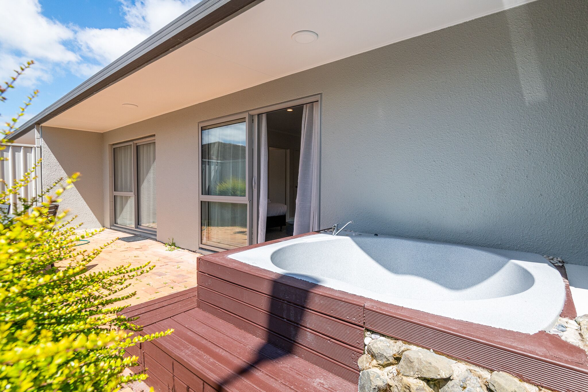 Une maison moderne dotée d’un grand jacuzzi extérieur, de portes-fenêtres coulissantes et d’une terrasse en bois.
