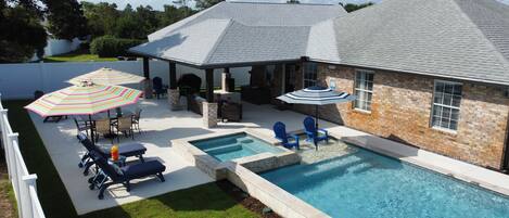 A backyard with a swimming pool, patio furniture, and a covered seating area.
