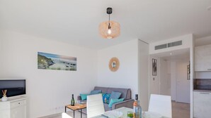 A modern living room with a dining table set for two, a sofa with cushions, a television, and a painting on the wall. - Le Diamanti by Interhome (Saint Aygulf)