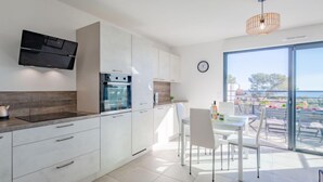 A modern kitchen with white cabinetry, a built-in oven, and a dining area with a glass table and chairs. - Le Diamanti by Interhome (Saint Aygulf)