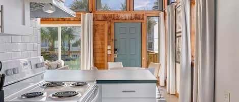 Una cocina moderna con una isla central, estufa y comedor con vista a palmeras.