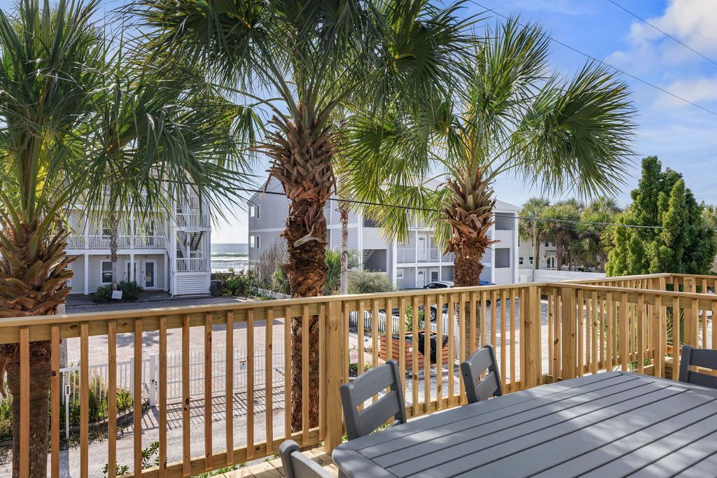 A wooden deck with a table and chairs, palm trees, and a view of white buildings with balconies.