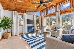 Un salon spacieux avec un plafond en bois, de grandes fenêtres et un tapis à rayures bleues.
