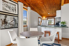A modern kitchen with white cabinets, a wooden ceiling, and a dining area with a round table and white chairs. - Dry Dock - 1BR/1BA Seagrove Beach Cottage - Sleeps 4 - Near Beach Access (Seagrove Beach)