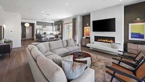 Ein modernes Wohnzimmer mit einer Eckcouch, einem Kamin, einem Flachbildfernseher und einem Essbereich im Hintergrund.