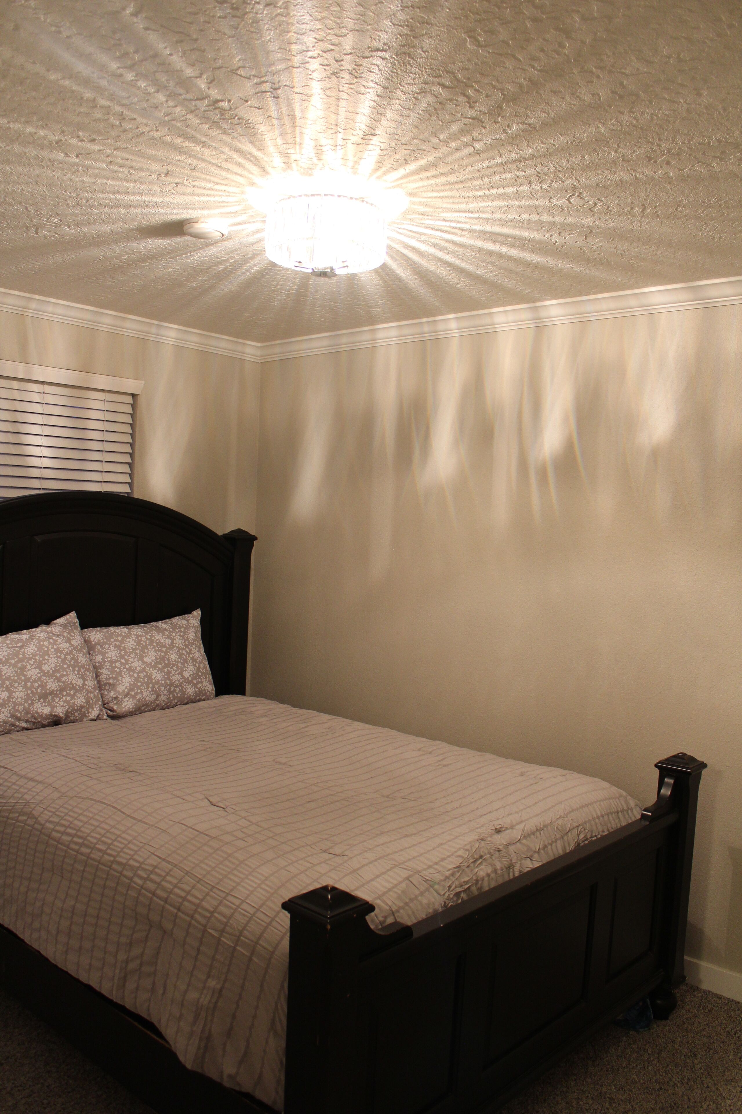 A bedroom with a bed, a headboard, a ceiling light, and a window with blinds.