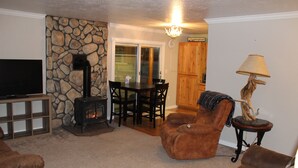 A living room with a stone wall, a fireplace, a television, and a dining area with chairs and a table. - Welcome to BarnRoots a Cozy Family sized house, bring your friends (Florence)
