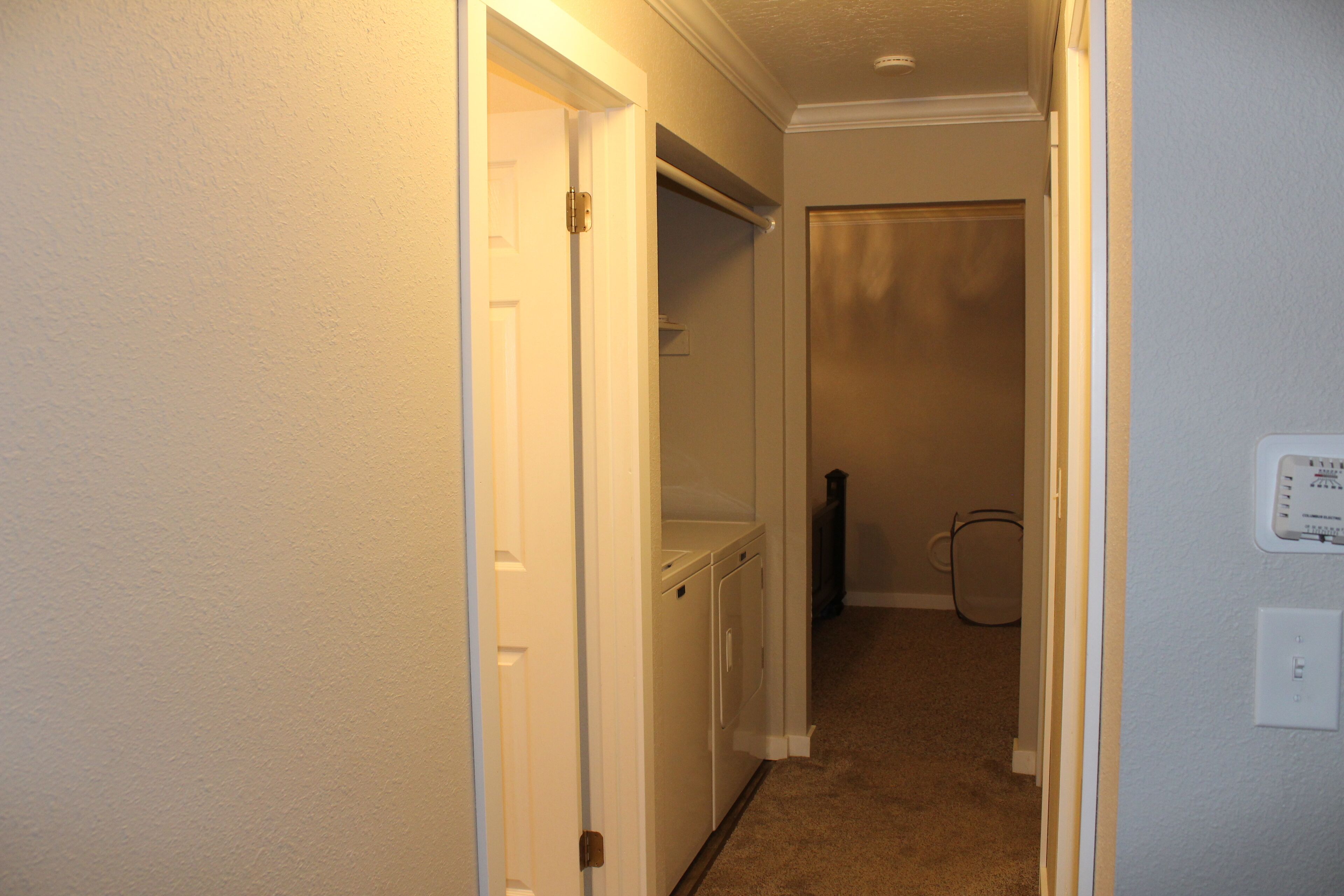 A hallway with a white door, a laundry area, and a thermostat on the wall.
