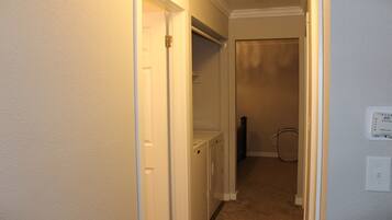 A hallway with a white door, a laundry area, and a thermostat on the wall.