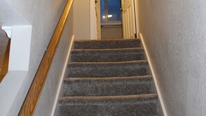 A carpeted staircase with wooden handrails, leading to a doorway with a light fixture above. - Welcome to BarnRoots a Cozy Family sized house, bring your friends (Florence)