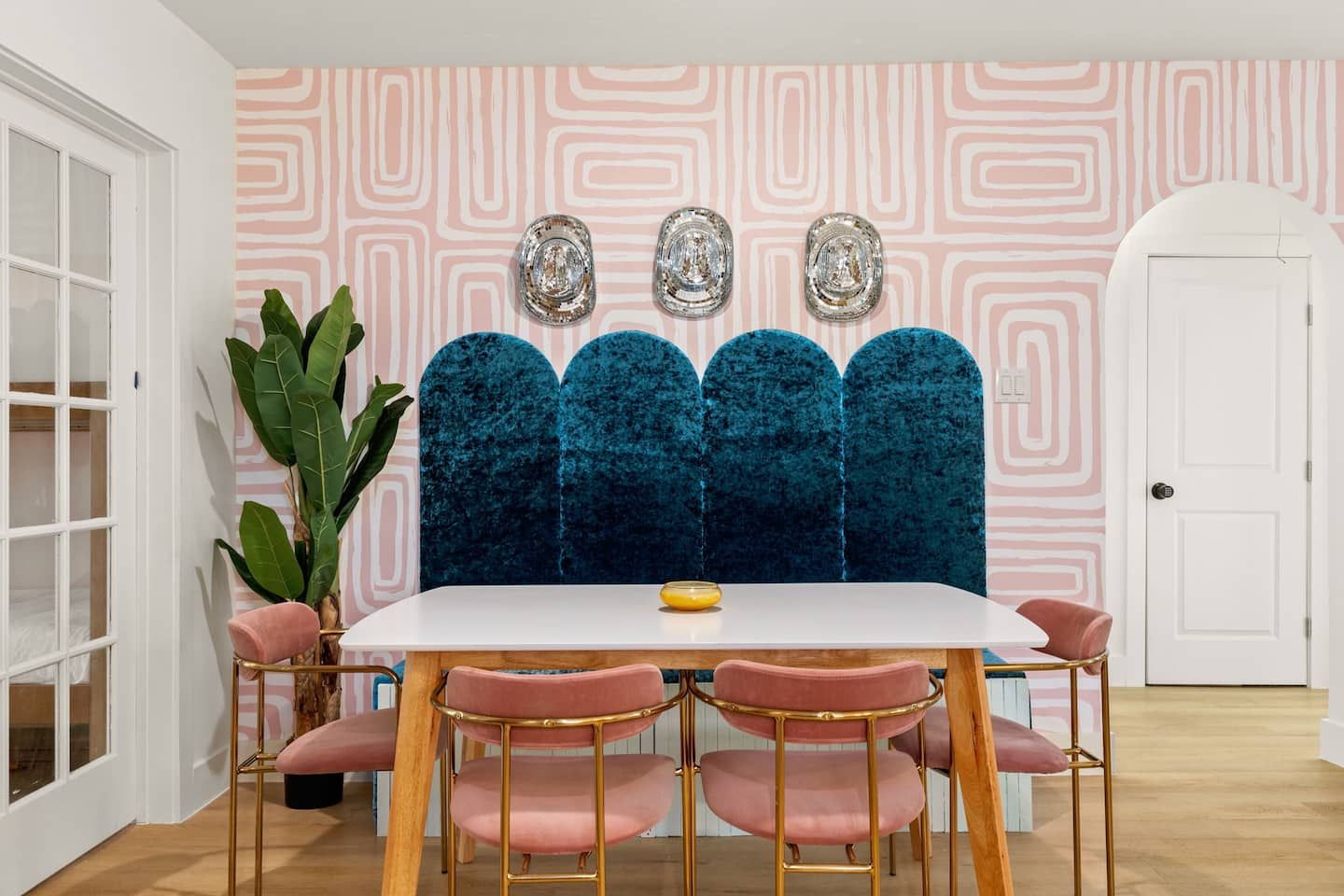 A dining area with a white table, pink chairs, and a blue velvet partition.
