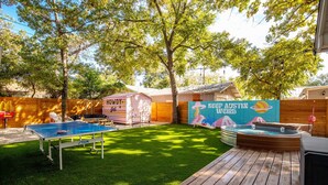 Een achtertuin met kunstgras, een tafeltennistafel, een jacuzzi en een houten terras.