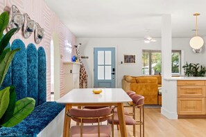 A modern living room with a blue sofa, a dining table with pink chairs, a giraffe sculpture, and a kitchen area with wooden cabinets. - BACH! Heated Pool/Sleeps 10/Firepit/2miles DT, ACL (Austin)