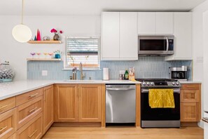 A modern kitchen with wooden cabinets, a stainless steel dishwasher, a gas stove, and a microwave. - BACH! Heated Pool/Sleeps 10/Firepit/2miles DT, ACL (Austin)