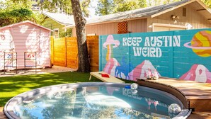 Een achtertuin met een jacuzzi, een houten omheining, een muur met de tekst 'KEEP AUSTIN WILD' en een kleine schuur.