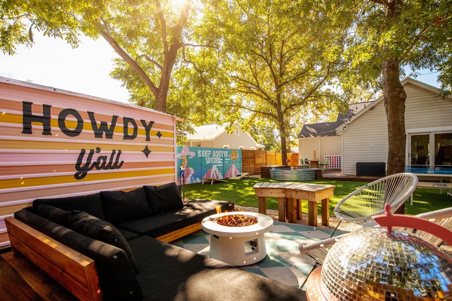 A backyard with a black sofa, a fire pit, a wooden table, and a disco ball.