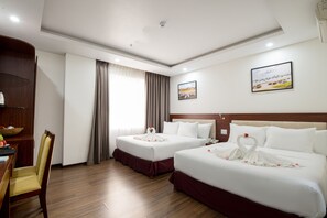 A hotel room with two beds, a wooden desk, a chair, a large window with curtains, and a framed picture on the wall. - Dao Ngoc Hotel (Da Nang)