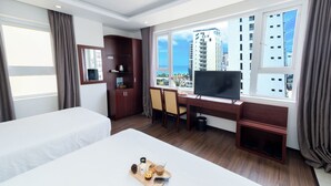 A hotel room with two beds, a desk with a TV, a window with a city view, and a small balcony. - Dao Ngoc Hotel (Da Nang)