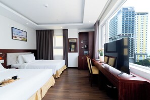Habitación de hotel con dos camas, un escritorio con televisor, un ventanal con vistas a la ciudad y un armario con artículos de aseo.